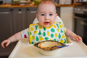 7 months old baby boy eating in a high chair