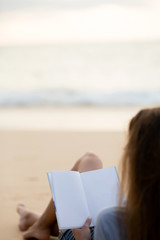 Fototapeta premium the brunette is lying on the beach in a shirt and denim shorts and reading an interesting book at sunset