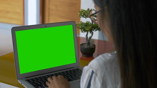 Over the shoulder shot of a business woman working looking at green screen. Office person using laptop computer with laptop green screen