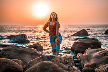 Lifestyle, a pretty brunette with red t-shirt and torn jeans on a sunset near the water with the sun behind