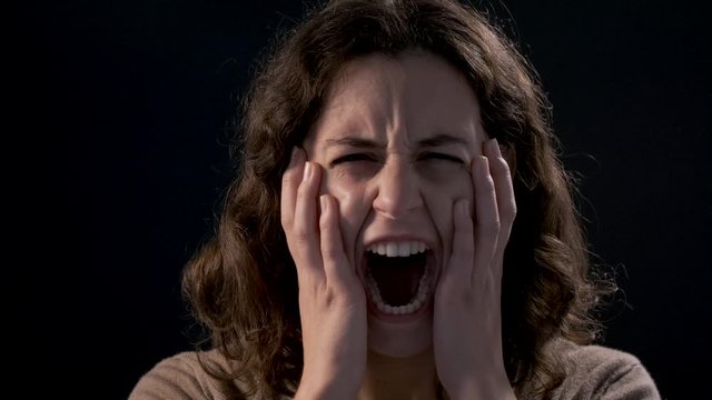 Video of a young woman close-up screaming on black background. Mental illness concept.