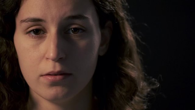 Video of sad young woman looking at camera on black background. Mental illness concept.