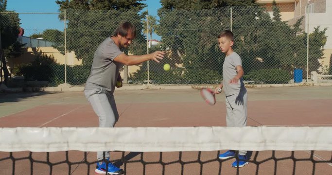 Child traning in tennis. Father and son practice blows in tennis on coart. Active leisure together.