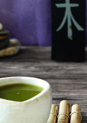 An authentic teawan bowl is filled with green tea and stands on bamboo sticks, with a surface with the hieroglyph 