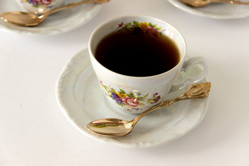 Black tea in a white cup and plate with a golden spoon
