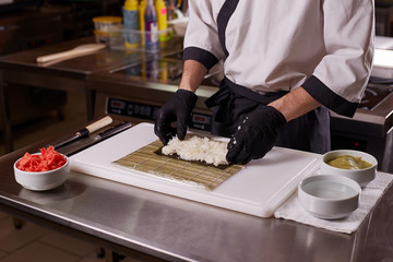 Process of making sushi and rolls at restaurant kitchen. Chefs hands with knife.