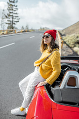 Lifestyle portrait of a carefree woman dressed casually in yellow sweater and red hat standing near...
