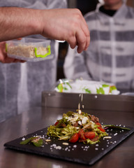 The process of cooking warm salad with veal. Hands of a chef in black gloves. Black slate board.