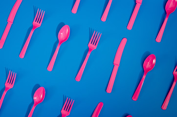 Flay lay photo of pink plastic disposable forks, spoons and knives lying on colorful background....