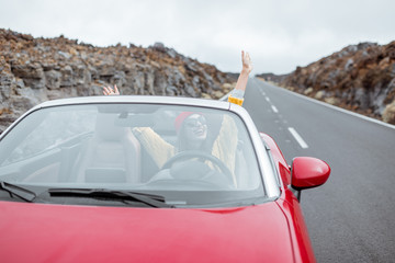 Portrait of a young woman traveling by convertible car on the picturesquare road on the volcanic valley. Carefree lifestyle and travel concept