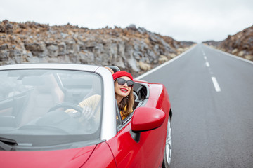 Portrait of a young woman traveling by convertible car on the picturesquare road on the volcanic...
