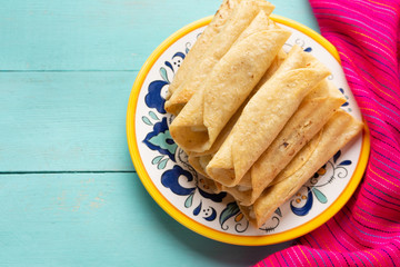 Mexican potato and cheese fried tacos also called flautas on turquoise background