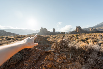 Woman pointing with hand on the volcanic mountains during a sunset, image focused on the background