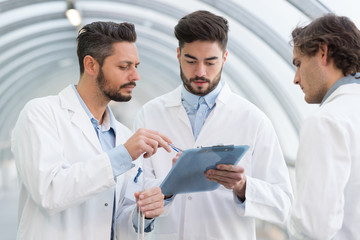 three men in labcoats looking at clipboard