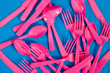 Flay lay photo of pink plastic disposable forks, spoons and knives lying on colorful background....