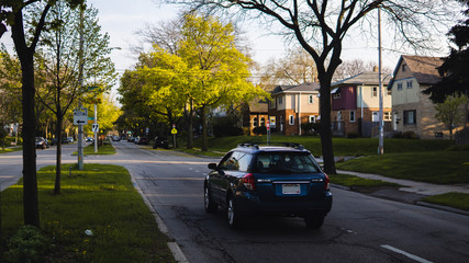 blue car driving down road during autumn on a sunny day