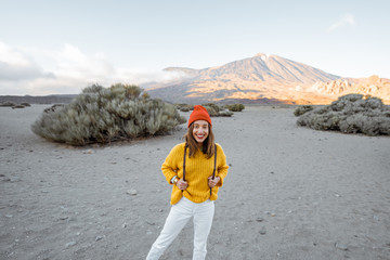 Portrait of a stylish woman in bright clothes on the beautiful volcanic valley with volcano on the background during a sunset. Traveling on Tenerife island, Spain