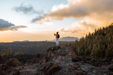 Woman photographing volcanic landscapes on a sunset while standing on the rocky land during the travel