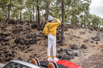 Young stylish woman traveling by car, enjoying beautiful landscapes while standing on the roadside...