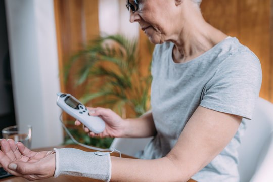 Senior Woman Doing Wrist Joint Physical Therapy with Conductive TENS Electrode Sock, Transcutaneous Electrical Nerve Stimulation