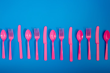 Flay lay photo of pink plastic disposable forks, spoons and knives lying on colorful background. Creative top view pattern.