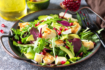Salad close-up with grilled chicken, avocado, brie cheese, arugula and pomegranate with vinaigrette dressing.