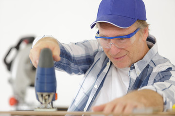 mature man carpenter builder working with electric jigsaw and wood