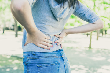 Closeup of young woman touching waist in park. Lady wearing hoodie and jeans, standing and touching...