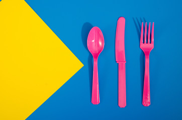 Flay lay photo of pink plastic disposable forks, spoons and knives lying on colorful background....