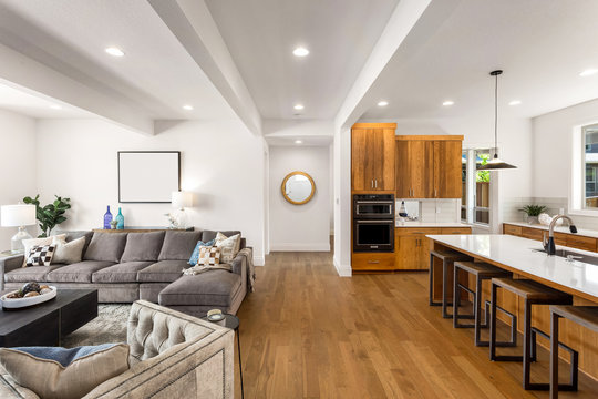 Living room and kitchen interior in new home with open concept floor plan. Kitchen features large island, hardwood floors, and stainless steel appliances. Living room is furnished