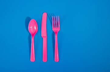 Flay lay photo of pink plastic disposable forks, spoons and knives lying on colorful background....
