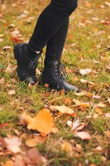 Women's black leather shoes stand on the ground covered with yellow autumn leaves. Lace up ankle boots for fall season.