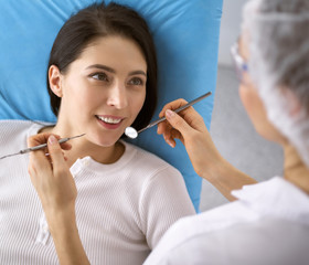 Smiling brunette woman being examined by dentist at dental clinic. Hands of a doctor holding dental instruments near patient's mouth. Healthy teeth and medicine concept