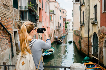 Fototapeta na wymiar Young woman taking a photo on her smartphone of a canal in Venice, Italy