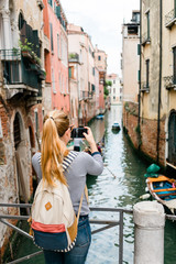 Fototapeta na wymiar Young woman taking a photo on her smartphone of a canal in Venice, Italy