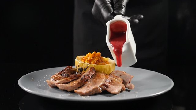 Restaurant meat dish cooking. Fine cuisine. Pouring with red cowberry sauce on sliced meat served on plate in slow motion. Shot in hd