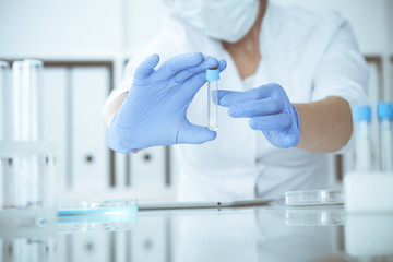 Close-up of professional female scientist in protective eyeglasses making experiment with reagents...