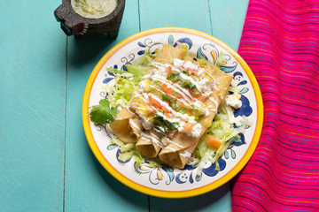 Mexican potato and cheese fried tacos also called flautas with green sauce on turquoise background