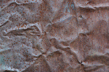 Close-up view of the crumpled rusty iron sheet with remnants of old paint and rust spots. Full frame image of the old weathered metal for texture or background, copy space