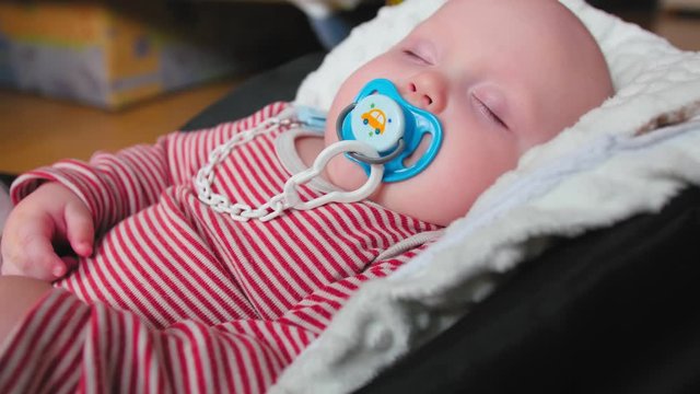 The little baby sleeps in car seat at home. Red white zip romper.