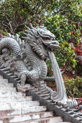 Dragon statue on the stairs against the background of flowers and greenery