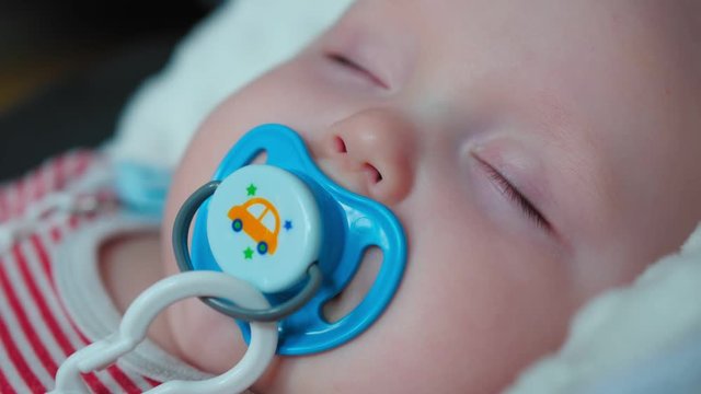 Portrait of sleeping baby with soother in mouth at home. Red white zip romper.