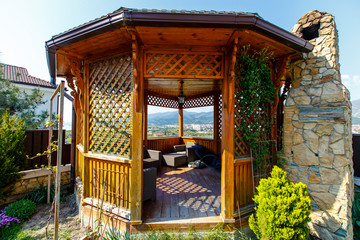 A wooden gazebo with a stone barbecue stove in the backyard of the cottage.  There is a green lawn...