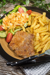 Fried pork chop in breadcrumbs, served with fries and salad.