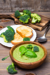 Ready to eat fresh hot broccoli puree soup with slices of broccoli and basil leaves in a wooden plate and slices of toasted white bread and spoon on a wooden table. Healthy eating and lifestyle.