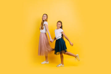 Mother and daughter holding hands walking, on an isolated yellow background