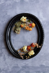 Composition of dried flowers, sprigs, leaves laid out inside black vintage oval frame on concrete cement background. Greeting card template, invitation. Happy mothers, women day, spring concept.