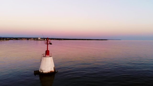 AERIAL: Beautiful sunset color reflection on the calm water. Passing a sea buoy. Umag, Croatia