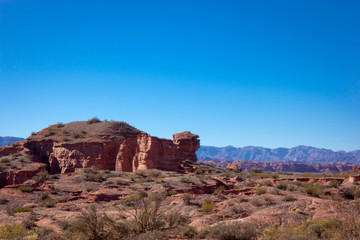 Red mountains in the desert with stone rock formations trees and green blue sky