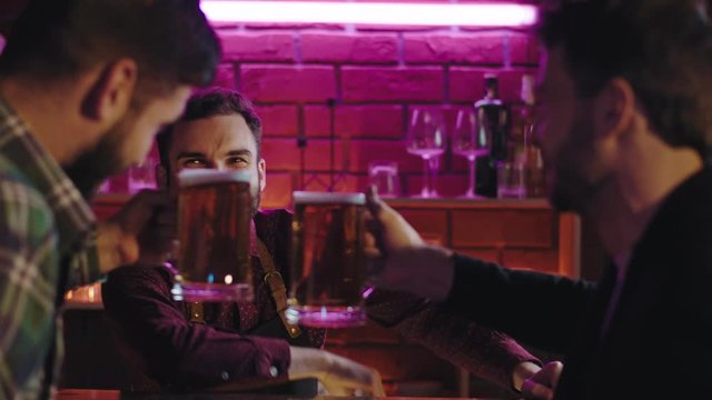 Happy and good looking bartender in a modern pub giving to big glasses of beer to his cu on a bar table